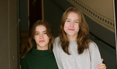 Ronja och Milla står i en lägenhetsport.